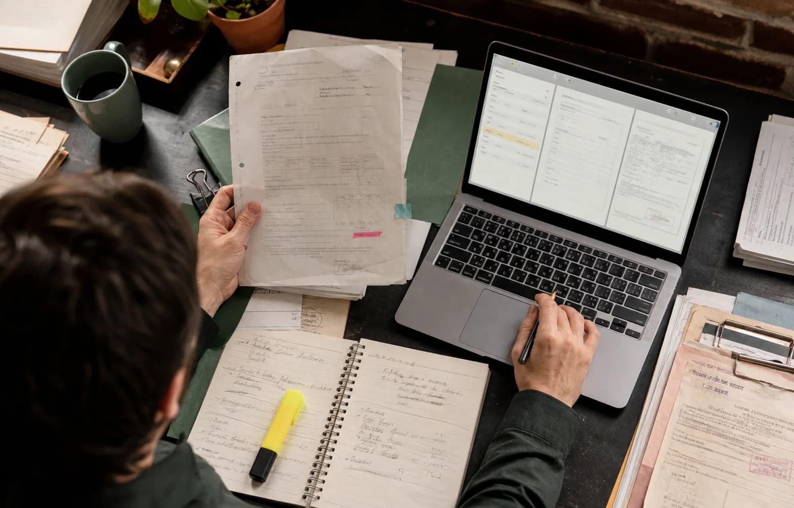 Person reviewing paper documents beside a document workflow on a laptop